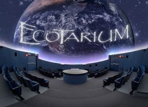 Photo of the EcoTarium in Worcester, MA. It shows a medium sized planetarium with 4 rows of theater seating with a panorama of Earth projected on the planetarium screen/ceiling with the EcoTarium logo across the image of Earth.
