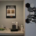 Coffee station with granite countertop with cups and a coffee machine. On the wall to the right is a photo board that resembles a honeycomb with various polaroid pictures pasted