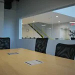Large conference room with window that spans the entire room looking out to a hallway with a staircase
